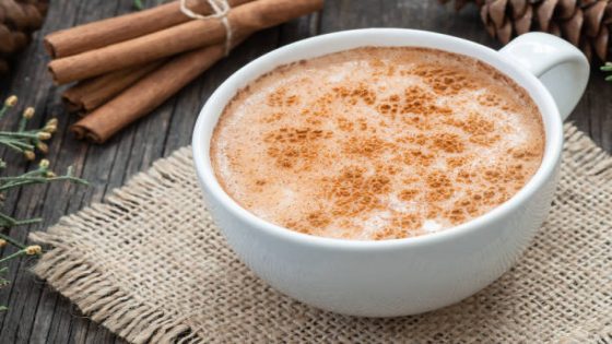 white cup of salep milky traditional hot drink of Turkey with cinnamon powder and sticks on rustic vintage wooden table. Sahlep background